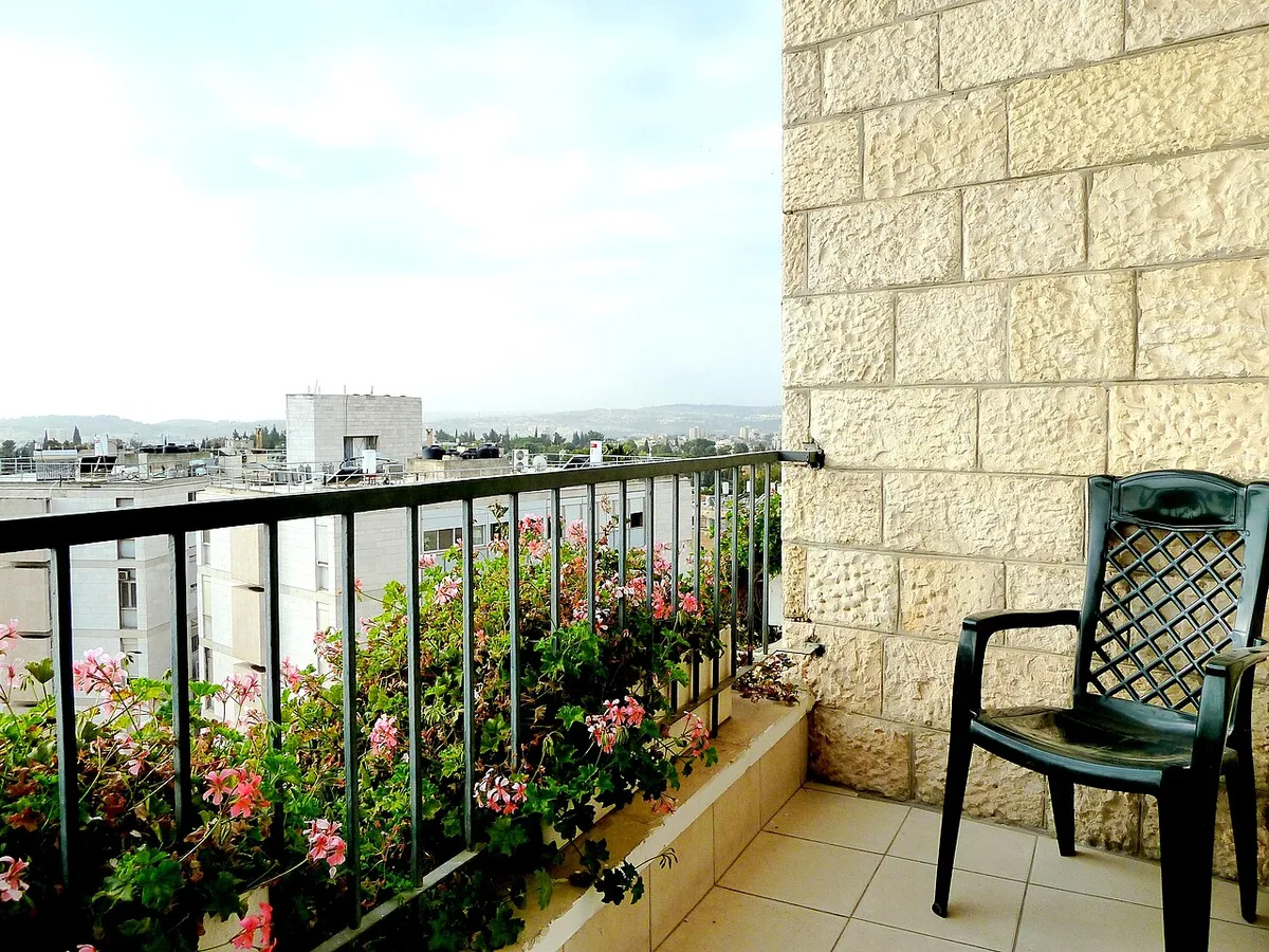 Kleiner Balkon mit blühenden Pelargonien am Geländer, Blick über die Dächer der Stadt