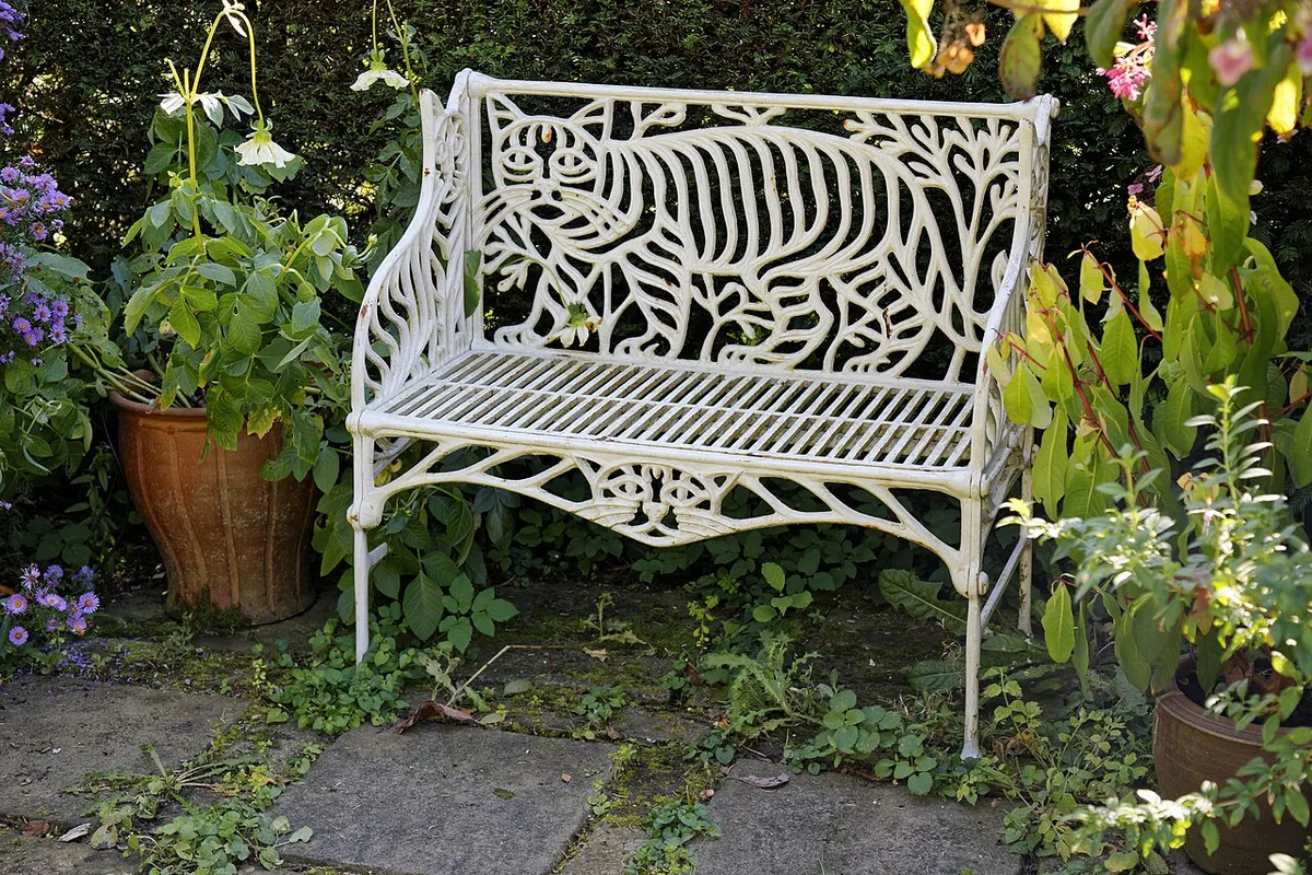 Weiße gusseiserne Gartenbank mit Katzenmotiv zwischen Pflanzen